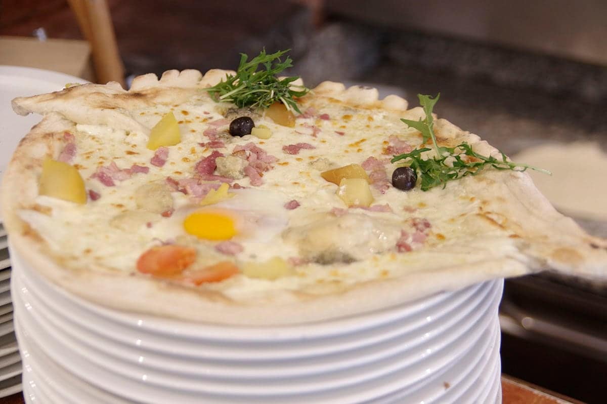 Pizza Dauphinoise, recette crémeuse : pommes de terre, lardons, œuf et roquette.